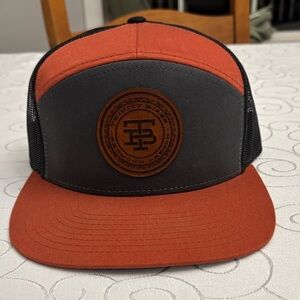 Orange and charcoal mesh-back trucker hat with a leather patch logo